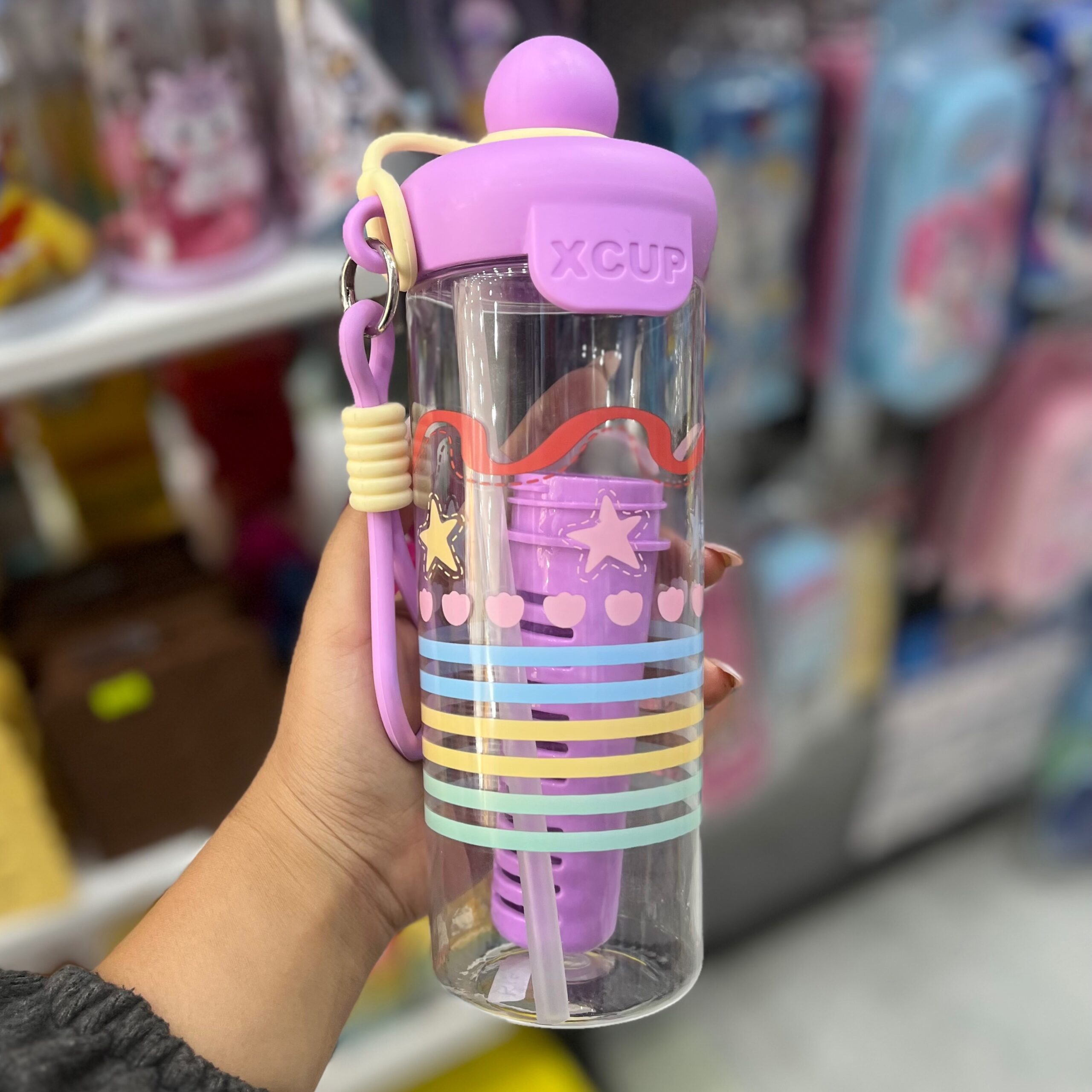 Termo cooler lila con infusor de sabores sostenido en mano dentro de una tienda